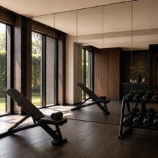 Luxe fitnessruimte met verzilverd blanke spiegelwand, dumbbellrek en fitnessbank.