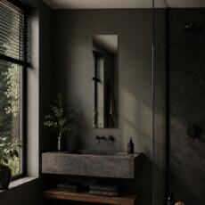 Smalle rechthoekige spiegel boven een natuurstenen wastafel in een donkere moderne badkamer.