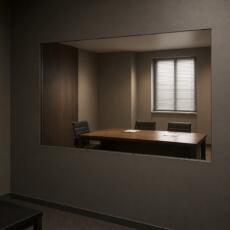 Doorkijkspiegel in een donkere observatieruimte met zicht op een moderne vergaderruimte achter het glas.